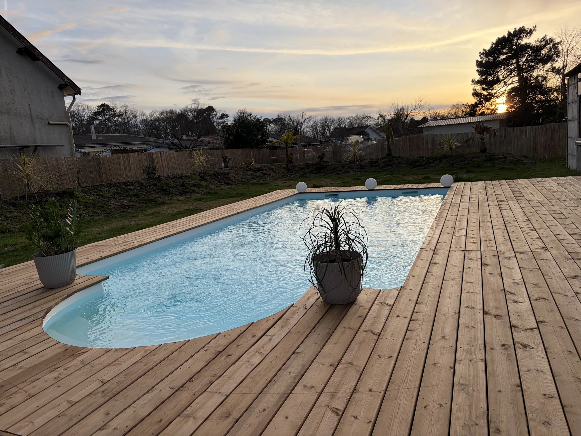Grande terrasse en pin traité autour d’une piscine ovale dans un jardin à Cazaux